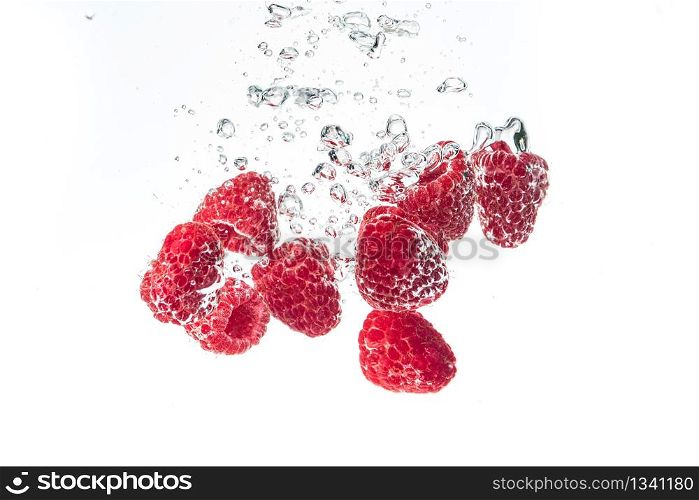 Raspberries splashing into crystal clear water with air bubbles