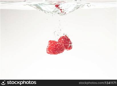 Raspberries splashing into crystal clear water with air bubbles background