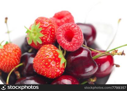 raspberries, strawberries and cherries in a bowl isolated on white