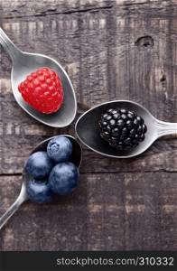 Raspberry blueberry and blackberry on spoon and wooden table. Still life photography