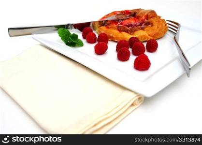 Raspberry Danish Pastry. Raspberry Danish pastry with fresh raspberries and a mint garnish served on a square white plate with fork, knife and a cloth napkin