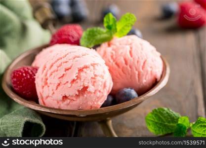 Raspberry ice cream scoops in copper bowl with forest berries and mint decoration. Summer food concept. Macro shoot.. Raspberry ice cream in copper bowl.