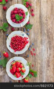 raspberry , red currant and strawberry with green leaves in cups, top view