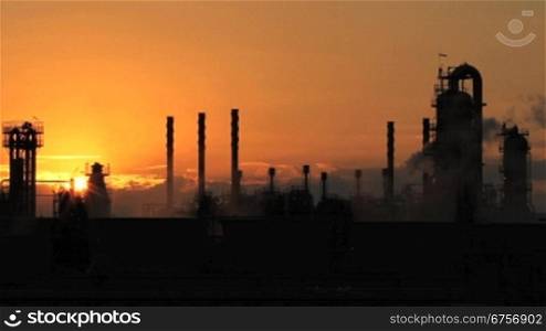Rauchende Industrieanlage steht im Schattenlicht in der auf-/bzw. untergehenden Sonne