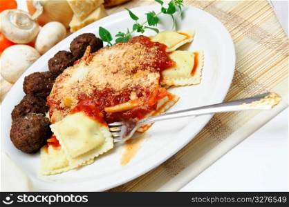 Ravioli. Ravioli topped with spaghetti sauce and Parmesan cheese with meatballs on the side served on a white plate garnished with a sprig of Oregano.