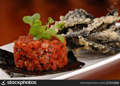 Raw ahi tuna tartare appetizer atop a sheet of nori and garnished with fresh green sprouts. Served with a side of tempura tortilla chips.