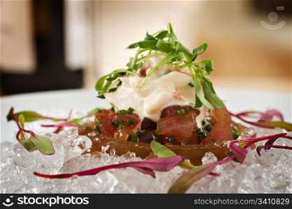 Raw ahi tuna tartare appetizer topped with seafood crab salad over ice and garnished with fresh green sprouts. Served with a side of tempura tortilla chips