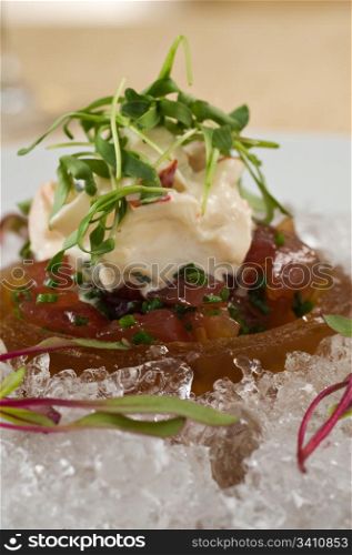 Raw ahi tuna tartare appetizer topped with seafood crab salad over ice and garnished with fresh green sprouts. Served with a side of tempura tortilla chips