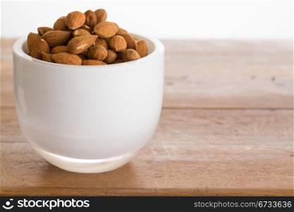Raw almond nuts in white glass bowl on old wooden table