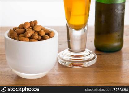 Raw almond nuts in white glass bowl on old wooden table with glass of cold beer