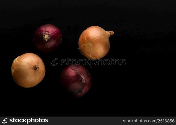 raw and unpeeled onion in red and golden colors on black background top view. a few raw onions on black background