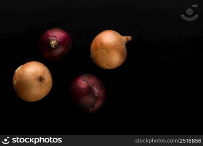 raw and unpeeled onion in red and golden colors on black background top view. a few raw onions on black background