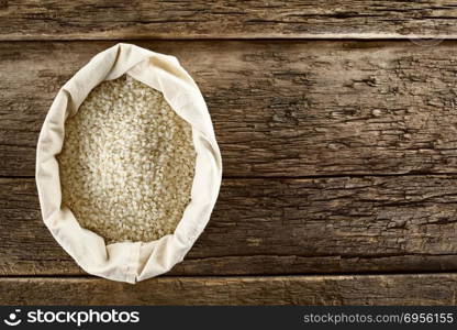 Raw arborio risotto short-grain rice in bag, photographed overhead on wood (Selective Focus, Focus on the rice) . Raw Arborio Risotto Rice