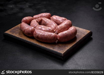 Raw barbecue sausages on a wooden cutting board with spices and vegetables. Free space for your text. Raw barbecue sausages on a wooden cutting board with spices and herbs