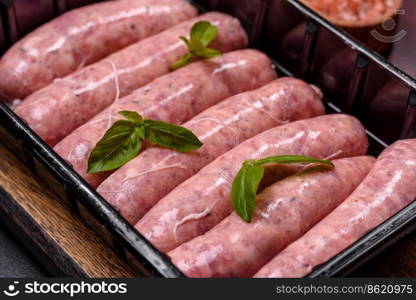 Raw barbecue sausages with spices and herbs. Free space for your text. Raw sausages with ingredients on a cutting board on a dark concrete background with copy space