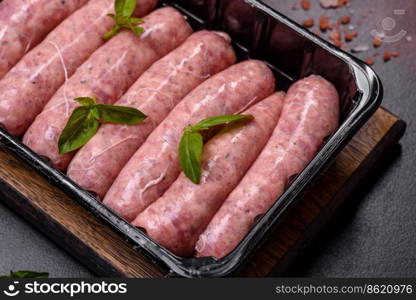 Raw barbecue sausages with spices and herbs. Free space for your text. Raw sausages with ingredients on a cutting board on a dark concrete background with copy space