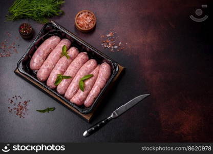 Raw barbecue sausages with spices and herbs. Free space for your text. Raw sausages with ingredients on a cutting board on a dark concrete background with copy space