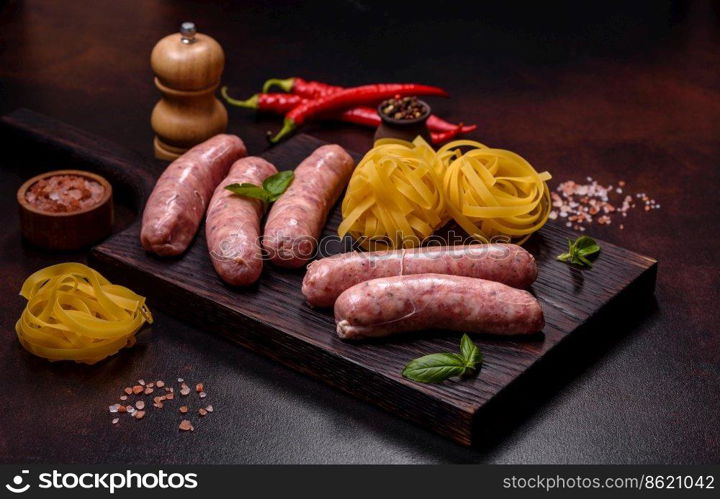 Raw barbecue sausages with spices and herbs. Free space for your text. Raw sausages with ingredients on a cutting board on a dark concrete background with copy space