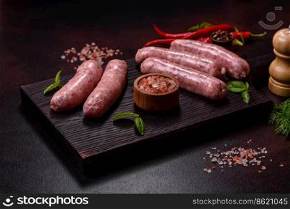Raw barbecue sausages with spices and herbs. Free space for your text. Raw sausages with ingredients on a cutting board on a dark concrete background with copy space