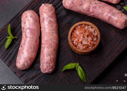 Raw barbecue sausages with spices and herbs. Free space for your text. Raw sausages with ingredients on a cutting board on a dark concrete background with copy space