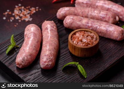 Raw barbecue sausages with spices and herbs. Free space for your text. Raw sausages with ingredients on a cutting board on a dark concrete background with copy space