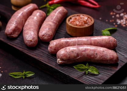 Raw barbecue sausages with spices and herbs. Free space for your text. Raw sausages with ingredients on a cutting board on a dark concrete background with copy space