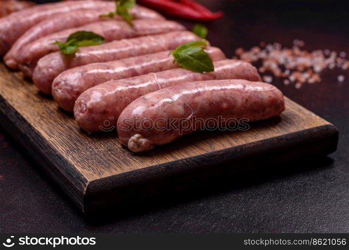 Raw barbecue sausages with spices and herbs. Free space for your text. Raw sausages with ingredients on a cutting board on a dark concrete background with copy space