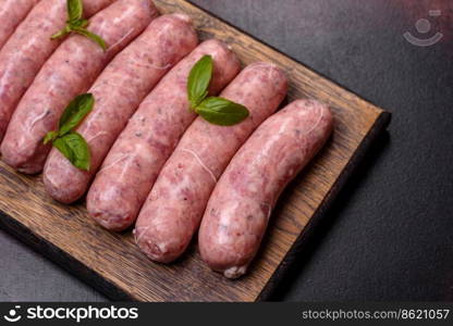 Raw barbecue sausages with spices and herbs. Free space for your text. Raw sausages with ingredients on a cutting board on a dark concrete background with copy space