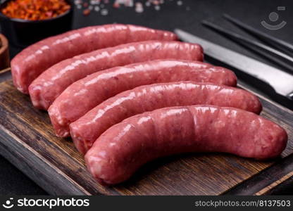 Raw barbecue sausages with spices and vegetables. Free space for your text. Raw sausages with ingredients on a cutting board on a stone background with copy space