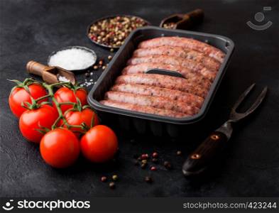 Raw beef and pork sausage in plastic tray with vintage knife and fork on black background.Salt and pepper with tomatoes