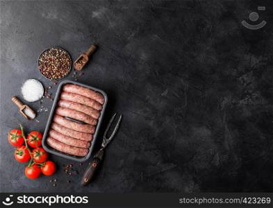 Raw beef and pork sausage in plastic tray with vintage knife and fork on black background.Salt and pepper with tomatoes and rosemary.