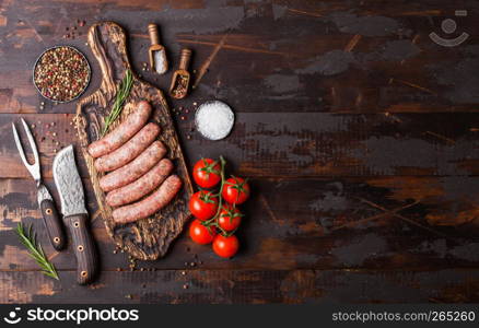 Raw beef and pork sausage on old chopping board with vintage knife and fork on wooden background.Salt and pepper with rosemary.