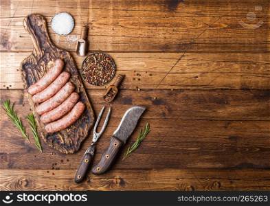 Raw beef and pork sausage on old chopping board with vintage knife and fork on wooden background.Salt and pepper with rosemary.