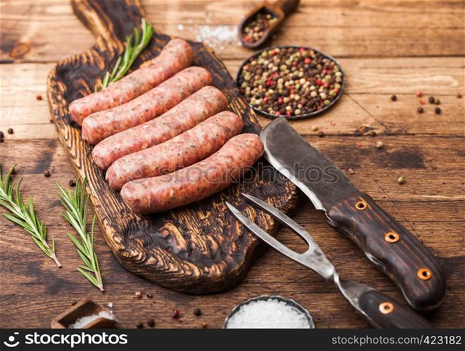 Raw beef and pork sausage on old chopping board with vintage knife and fork on wooden background.Salt and pepper.