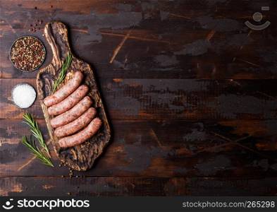 Raw beef and pork sausage on vintage chopping board with salt and pepper on wooden background.