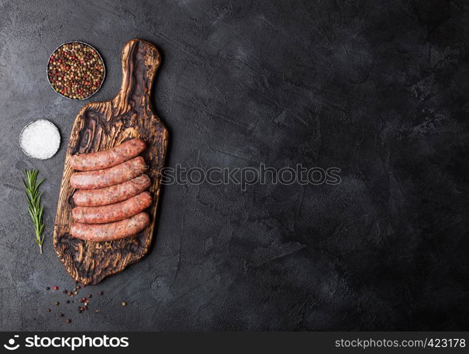 Raw beef and pork sausage on vintage chopping board with salt and pepper on black background.