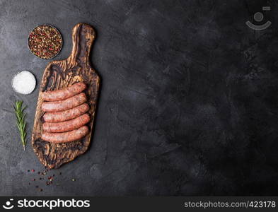 Raw beef and pork sausage on vintage chopping board with salt and pepper on black background.