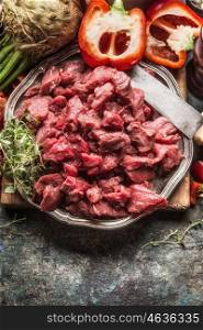 Raw beef chopped meat vegetables ingredient , kitchen knife and cooking pot . Stew or goulash preparation on dark rustic background, top view
