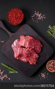 Raw beef cut into several pieces on a wooden cutting board on a dark concrete background
