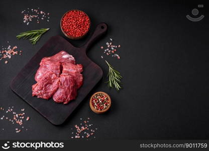 Raw beef cut into several pieces on a wooden cutting board on a dark concrete background