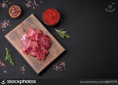 Raw beef cut into several pieces on a wooden cutting board on a dark concrete background