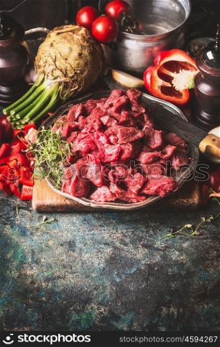 Raw Beef goulash of young bulls with vegetables and cooking ingredients on dark rustic background , preparation, border