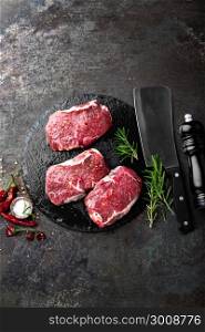 Raw beef meat. Fresh steaks on slate board on black background. Top view