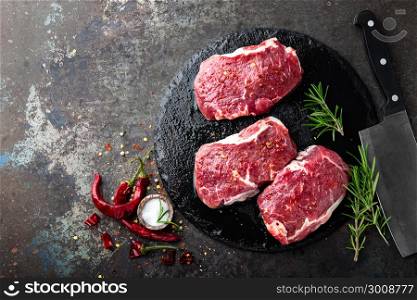 Raw beef meat. Fresh steaks on slate board on black background. Top view
