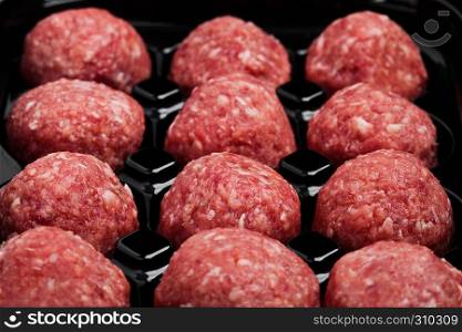 Raw beef meatballs in black plastick tray close up