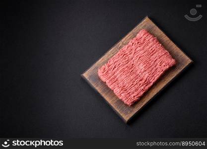 Raw beef or pork mince with salt spices and herbs on a wooden cutting board on a dark concrete background
