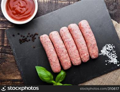 Raw beef sausages with salt and basil on stone board.Dark brown board. Salt and pepper on background