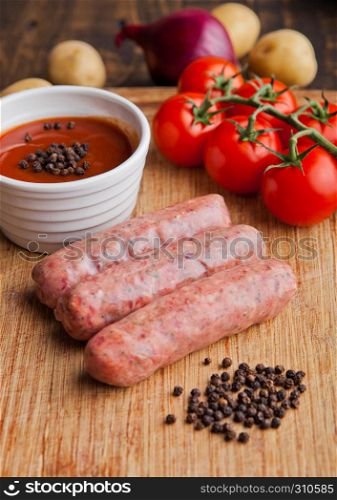 Raw beef sausages with tomatoes and sause on kitchen wooden board. Potatoes and pepper