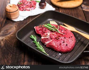 raw beef steak in spices on a black frying pan for grilling, close up