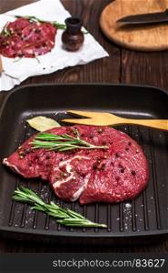 raw beef steak on a black frying pan with spices and rosemary branch, top view